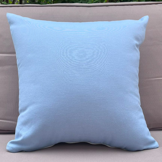 Light blue cushion cover displayed on a beige outdoor sofa in a garden patio setting