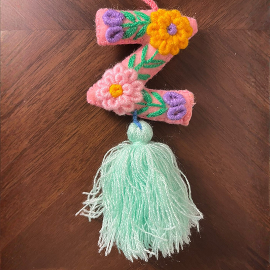 Handmade embroidered letter Z ornament with colorful floral stitching and light green tassel on wooden background