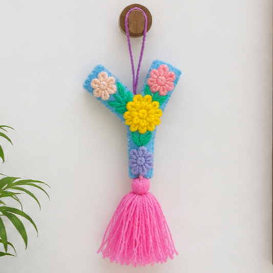 Handmade embroidered letter Y ornament with colorful floral stitching and bright pink tassel on wooden surface