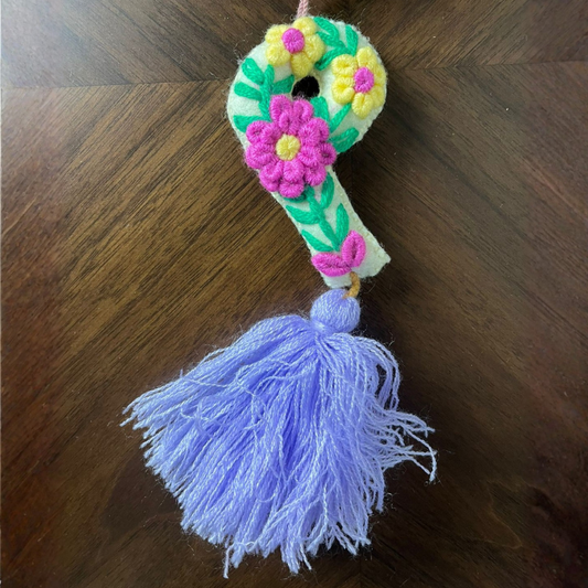 Handmade embroidered letter P ornament with colorful floral embroidery and lavender tassel on wooden background