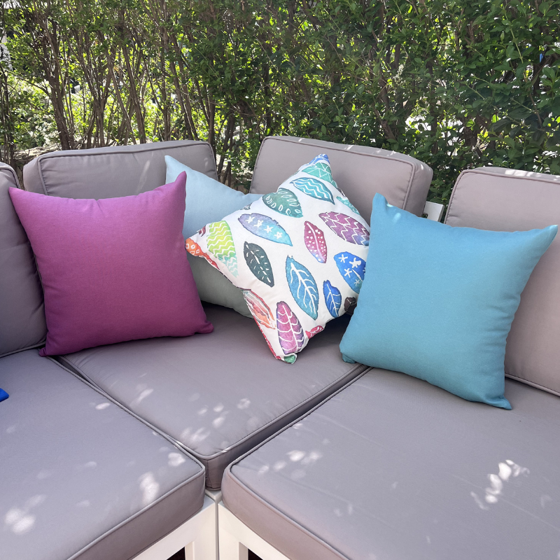Light blue cushion cover displayed on a beige outdoor sofa in a garden patio setting