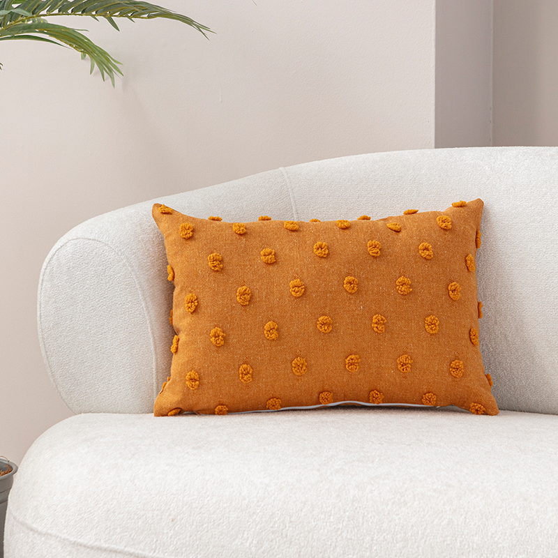 Mustard yellow textured cushion with raised knot-dot details placed on a light beige curved sofa.