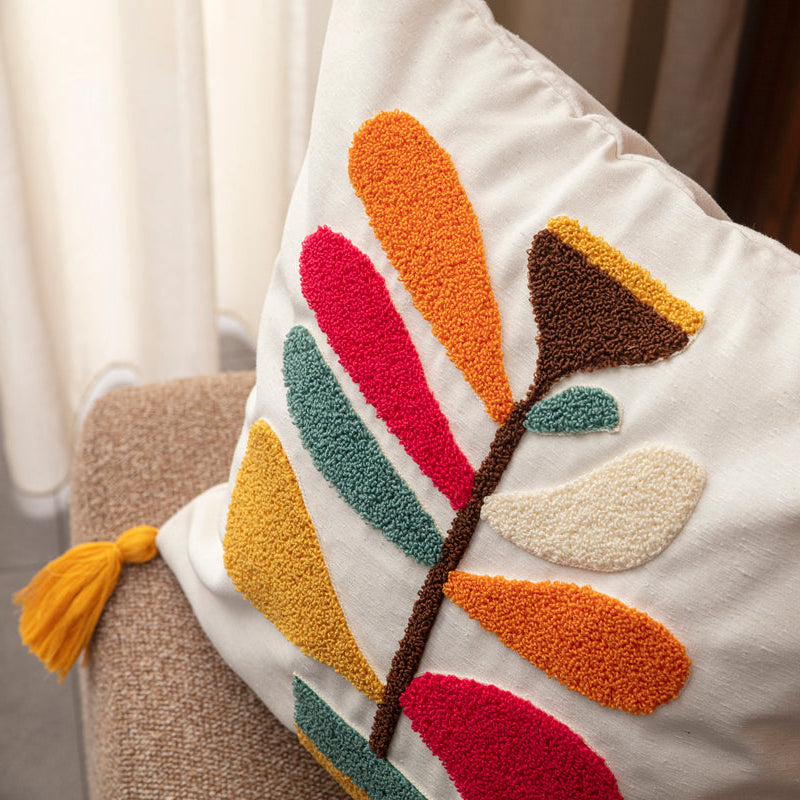 Cream cushion cover with colorful tufted leaf embroidery and yellow tassels on each corner