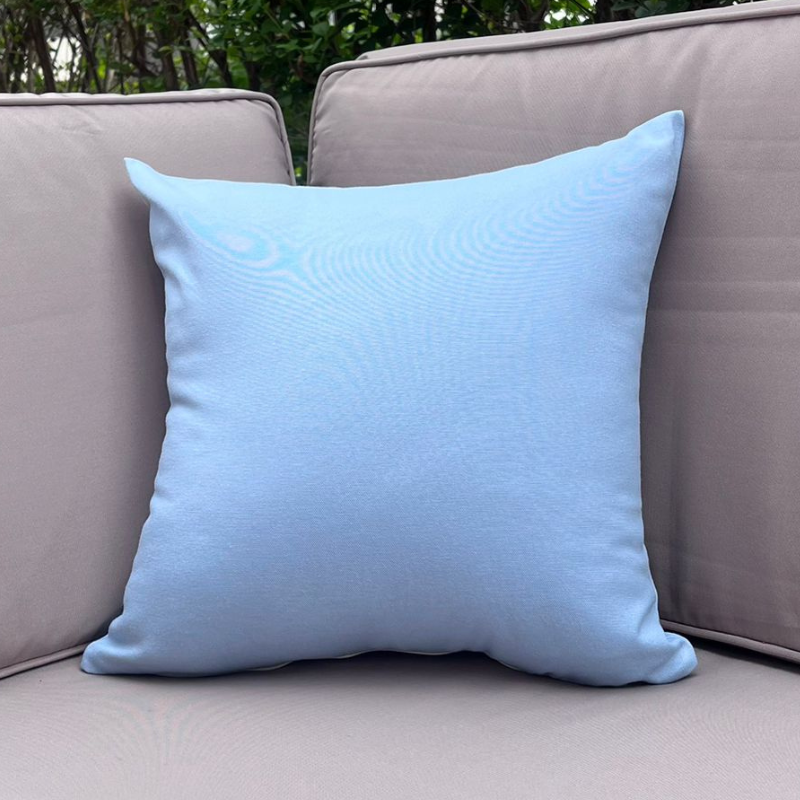 Light blue cushion cover displayed on a beige outdoor sofa in a garden patio setting