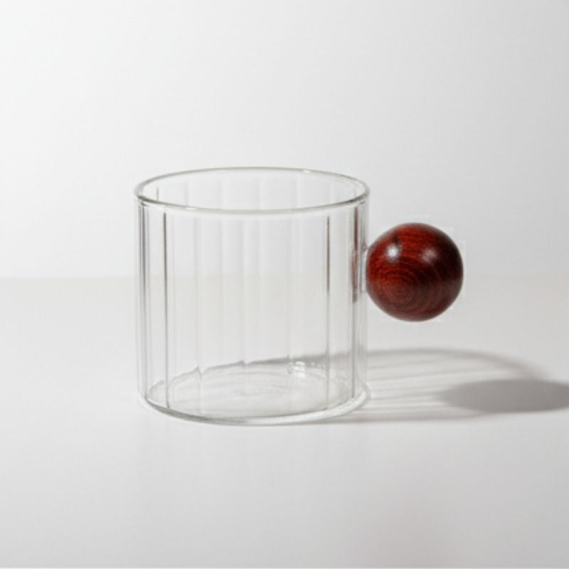 Ribbed glass mug with wooden ball handle on white background
Modern artistic coffee cup with ribbed glass body
Transparent glass mug with unique round wooden handle
Designer borosilicate glass mug for coffee or tea