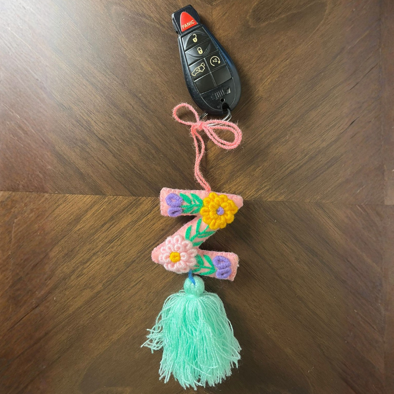 Handmade embroidered letter Z ornament with colorful floral stitching and light green tassel on wooden background