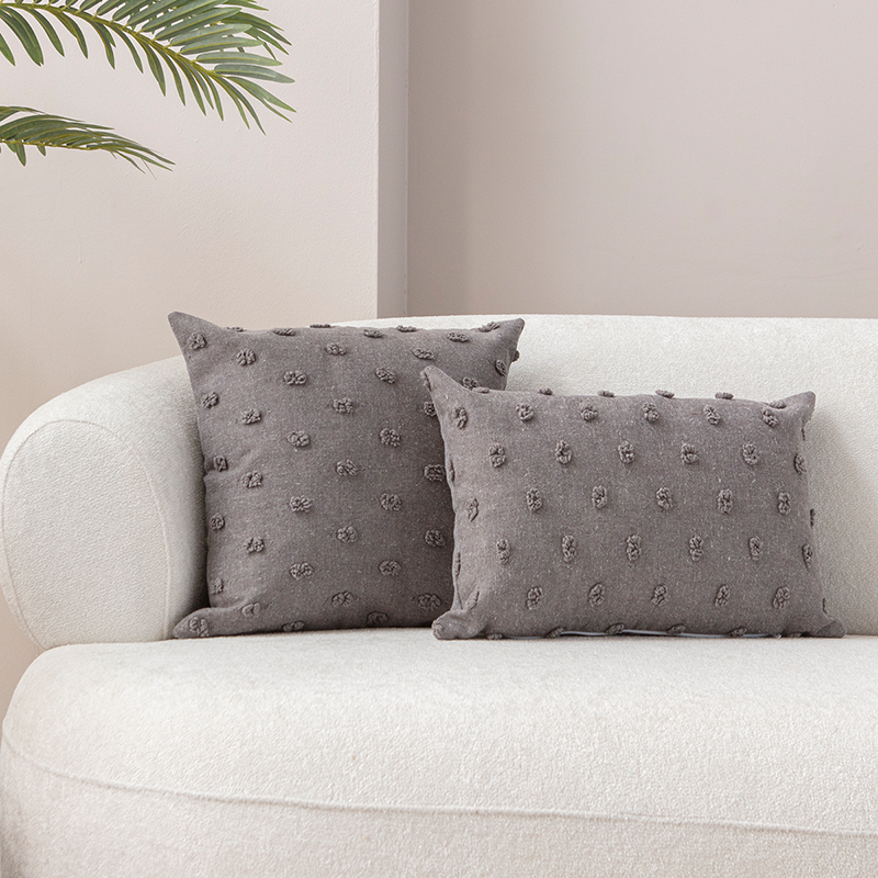 Taupe textured cushion with raised knot-dot details placed on a light beige curved sofa.