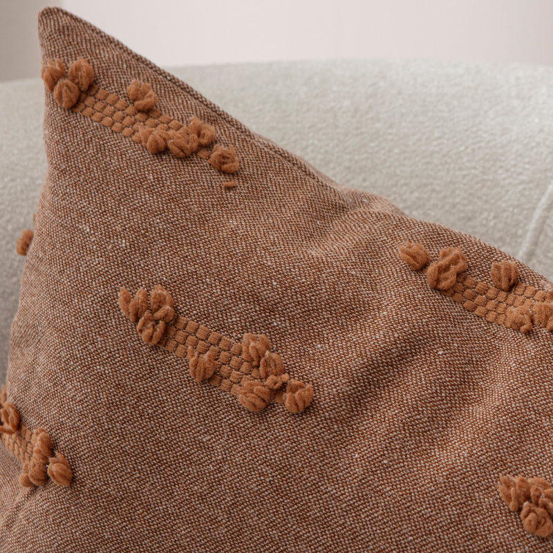 Warm brown woven textured throw pillow on light sofa – decorative cushion with horizontal tufted accents