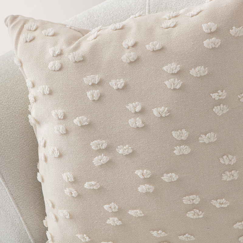 Beige textured cushion with raised knot-dot details displayed on a light curved sofa.
