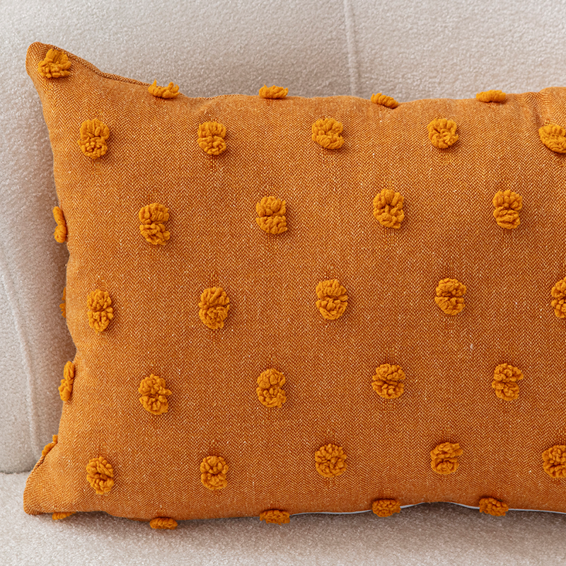 Mustard yellow textured cushion with raised knot-dot details placed on a light beige curved sofa.