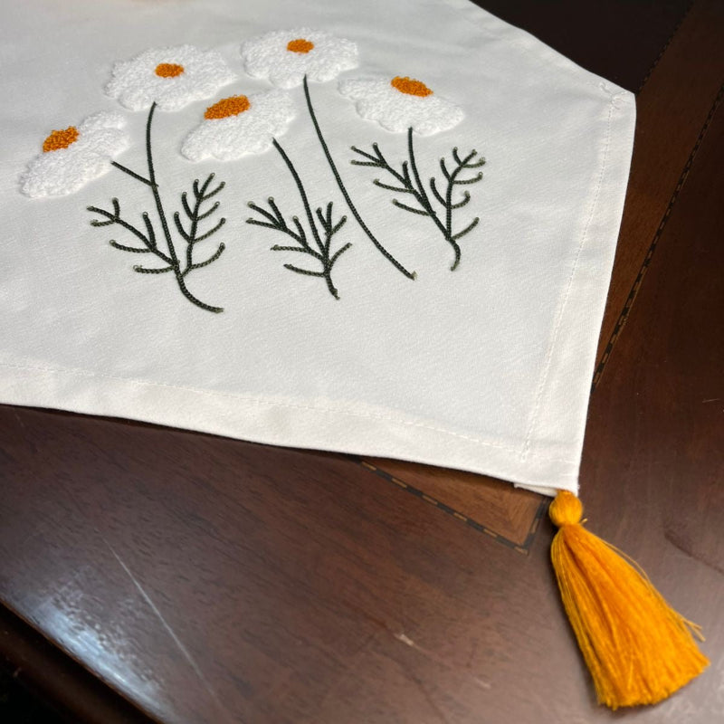 White cotton table runner with embroidered wildflowers and orange centers on wooden coffee table