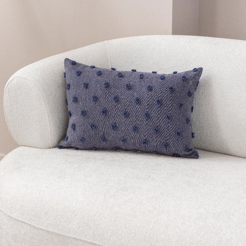 Blue textured cushion with raised knot-dot details placed on a light beige sofa.