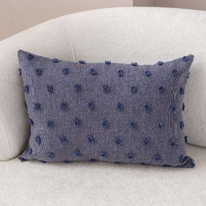 Blue textured cushion with raised knot-dot details placed on a light beige sofa.