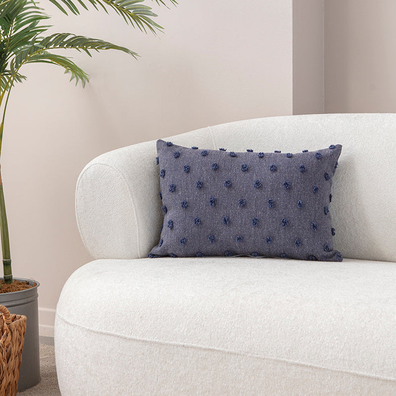 Blue textured cushion with raised knot-dot details placed on a light beige sofa.