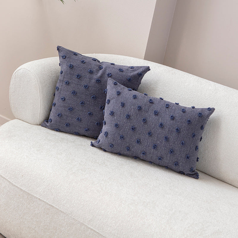 Blue textured cushion with raised knot-dot details placed on a light beige sofa.