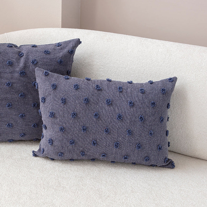 Blue textured cushion with raised knot-dot details placed on a light beige sofa.