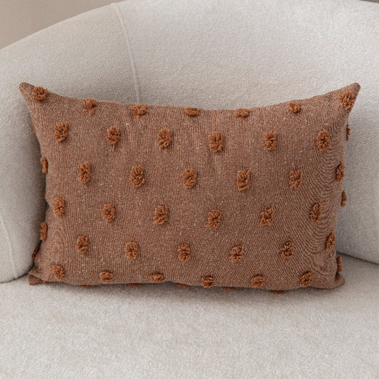 Terracotta textured cushion with handcrafted knot-dot details on a light beige sofa.
