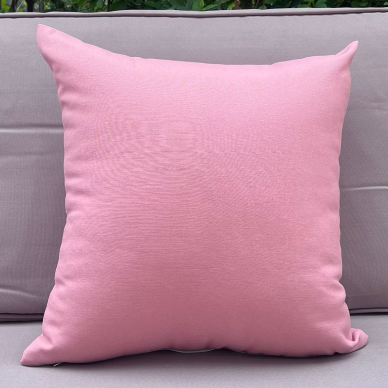 Light pink cushion cover displayed on a beige outdoor sofa in a garden patio setting