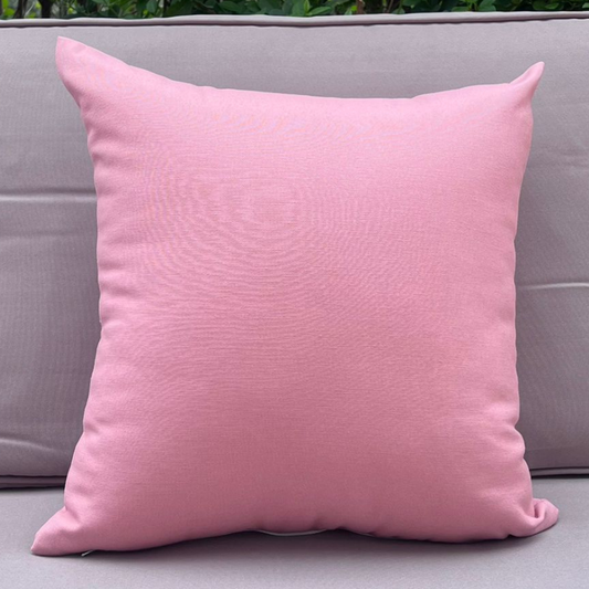 Light pink cushion cover displayed on a beige outdoor sofa in a garden patio setting