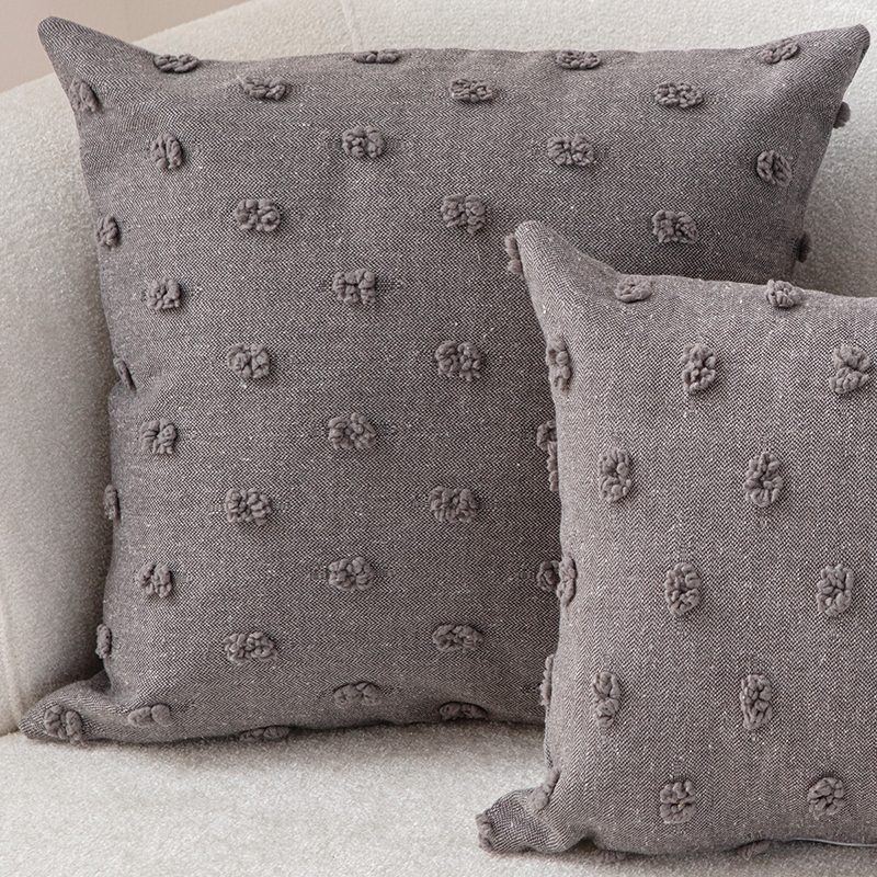 Taupe textured cushion with raised knot-dot details placed on a light beige curved sofa.