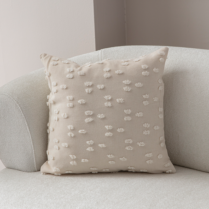 Beige textured cushion with raised knot-dot details displayed on a light curved sofa.