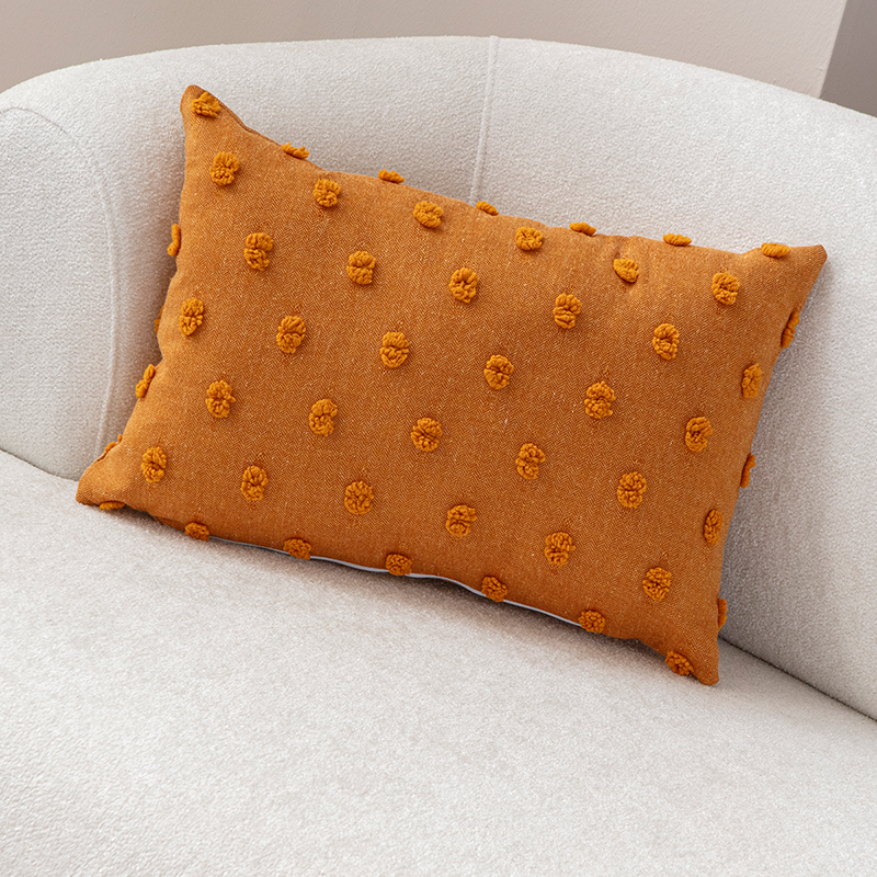 Mustard yellow textured cushion with raised knot-dot details placed on a light beige curved sofa.