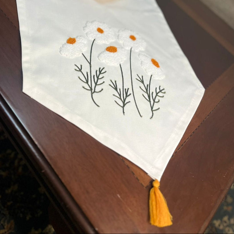 White cotton table runner with embroidered wildflowers and orange centers on wooden coffee table