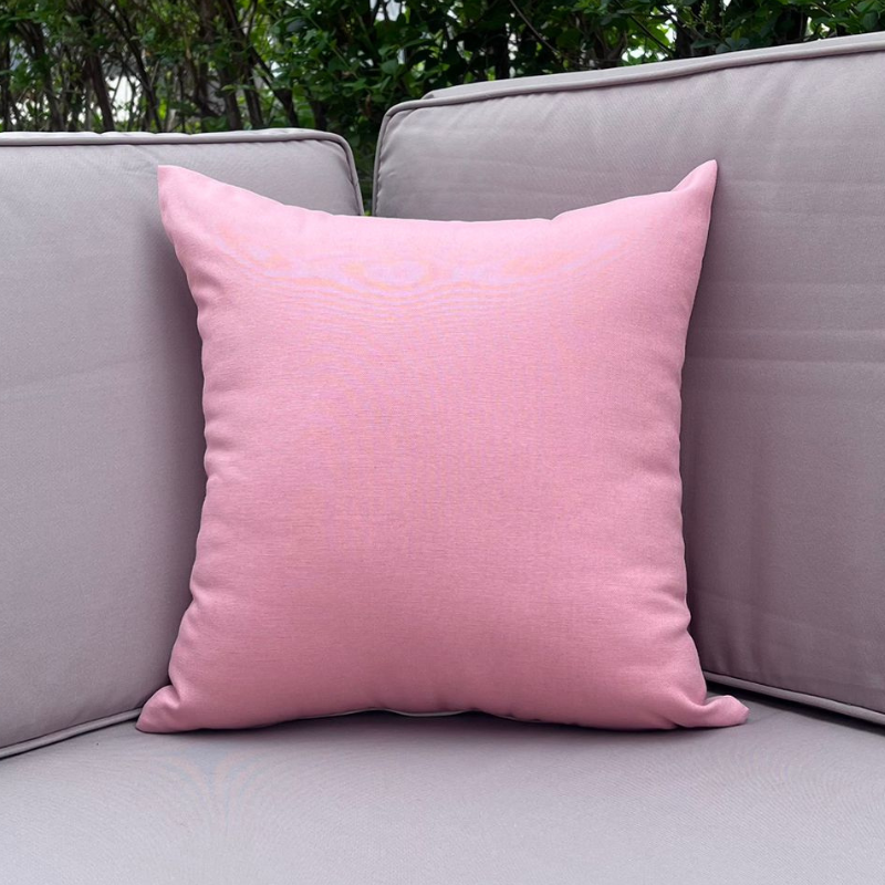 Light pink cushion cover displayed on a beige outdoor sofa in a garden patio setting