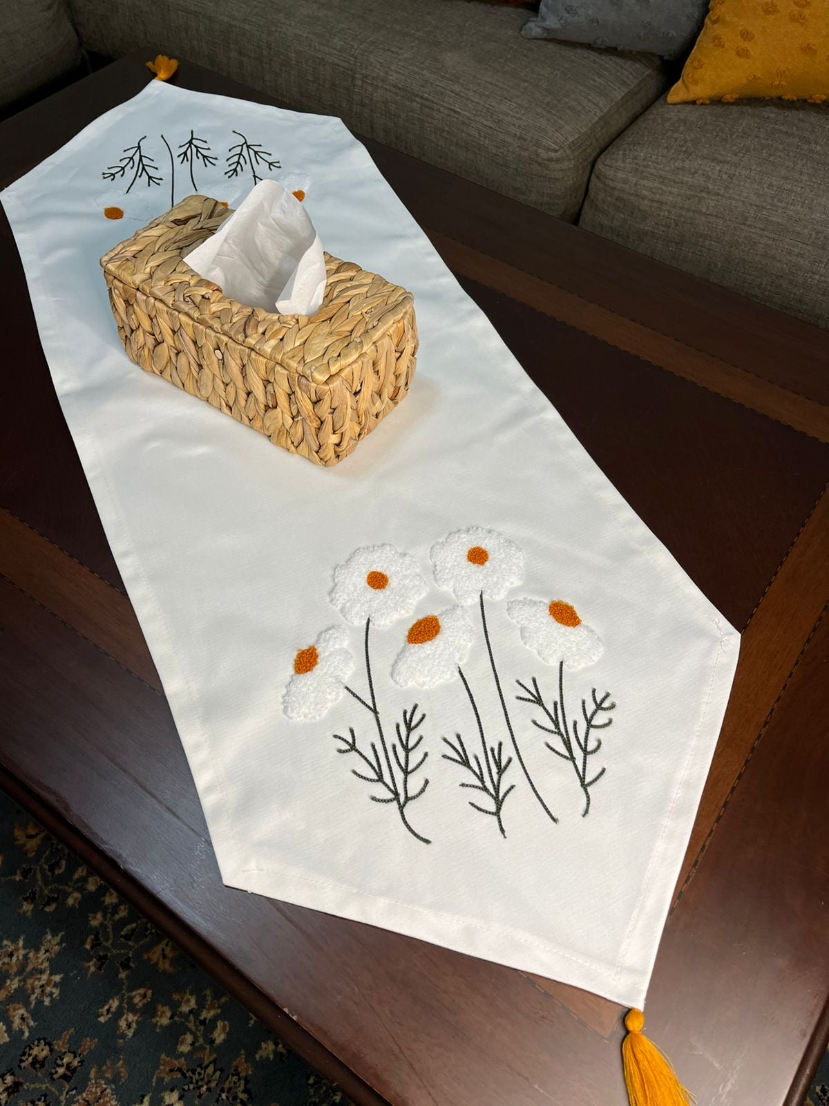 White cotton table runner with embroidered wildflowers and orange centers on wooden coffee table