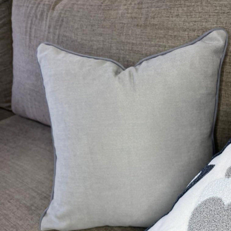 Embroidered floral cushion with navy and grey design, soft cream fabric, and tassel accents on each corner, perfect for home decor."