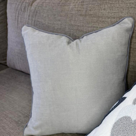 Embroidered floral cushion with navy and grey design, soft cream fabric, and tassel accents on each corner, perfect for home decor."