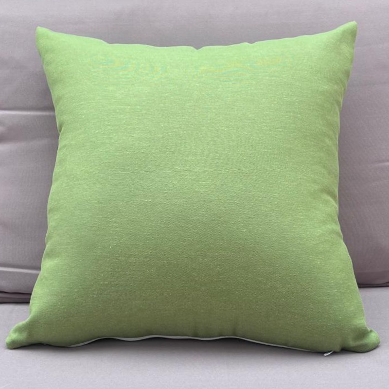 Plain green cushion cover displayed on an outdoor beige sofa in a garden setting