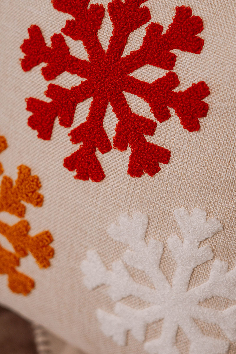 Beige cushion with embroidered snowflakes in white, red, and orange on a blue sofa – Autumn Bloom Collection