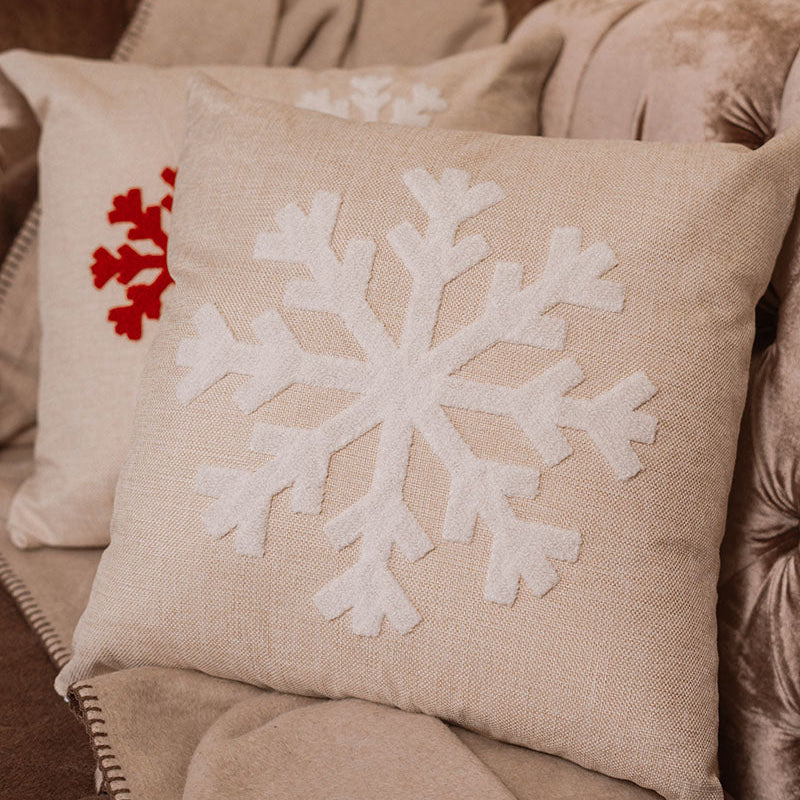 Beige cushion with raised white snowflake embroidery on a blue sofa – Autumn Bloom Collection