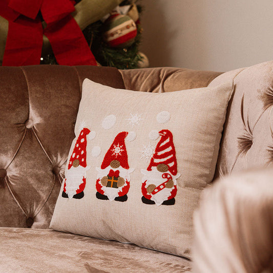Beige cushion with embroidered Christmas gnomes in red hats and white beards on a blue sofa – Autumn Bloom Collection