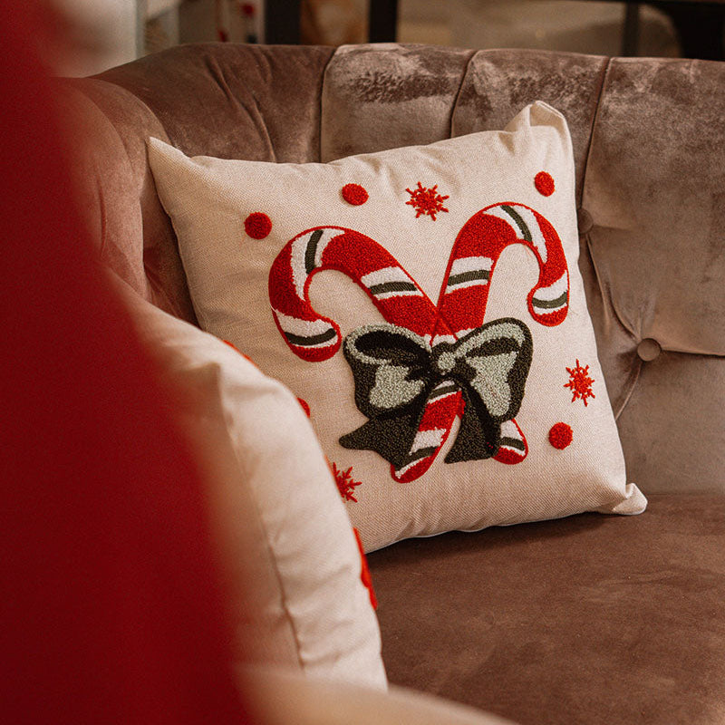 Beige cushion with embroidered red and white candy canes tied with a green bow on a blue sofa – Autumn Bloom Collection