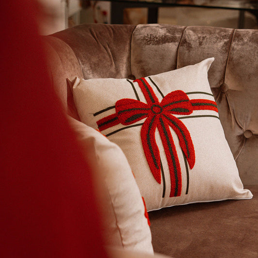 Beige cushion with embroidered red bow and ribbon gift design on a blue sofa – Autumn Bloom Collection