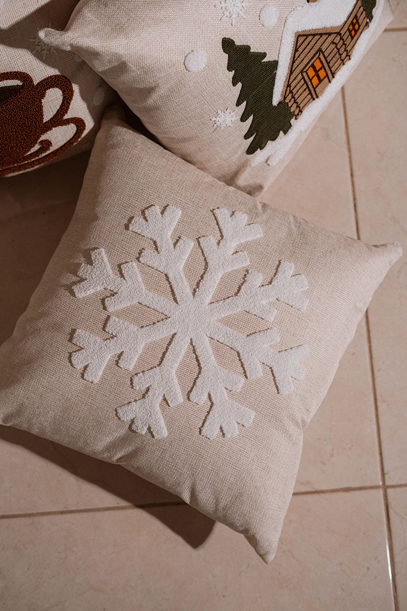 Beige cushion with raised white snowflake embroidery on a blue sofa – Autumn Bloom Collection