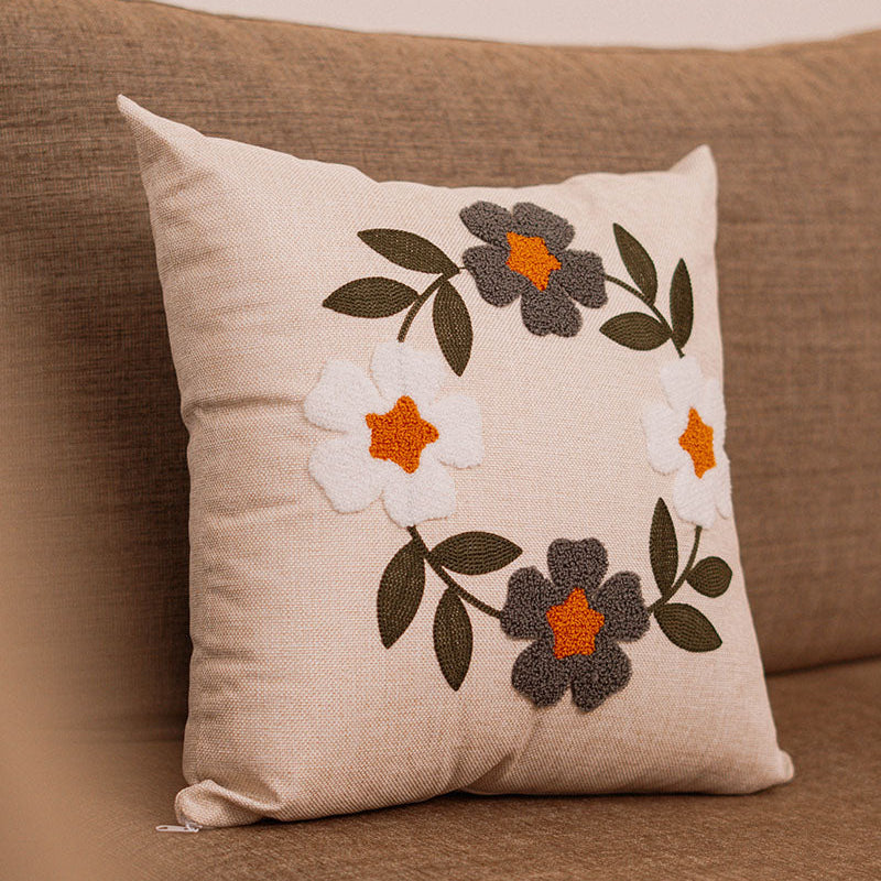 Hand-embroidered cushion with blue and rust flowers on beige fabric, placed on a blue sofa