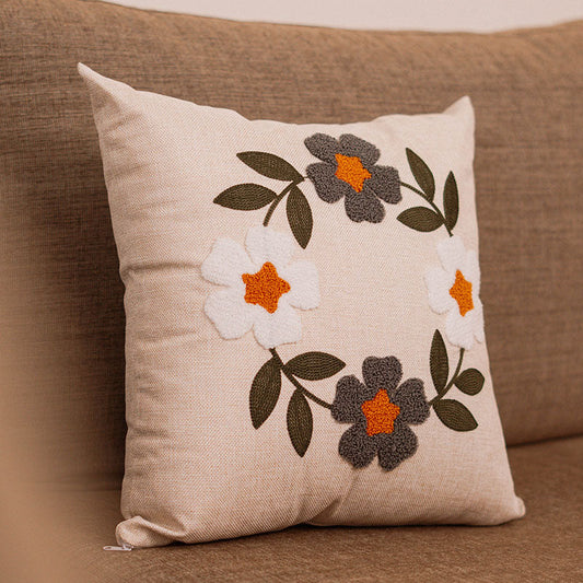 Hand-embroidered cushion with blue and rust flowers on beige fabric, placed on a blue sofa
