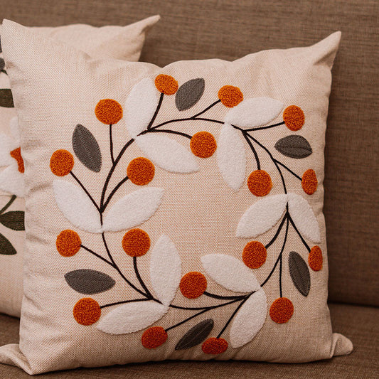 Beige cushion with embroidered autumn wreath of orange berries and white-grey leaves on a blue sofa – Autumn Bloom Collection