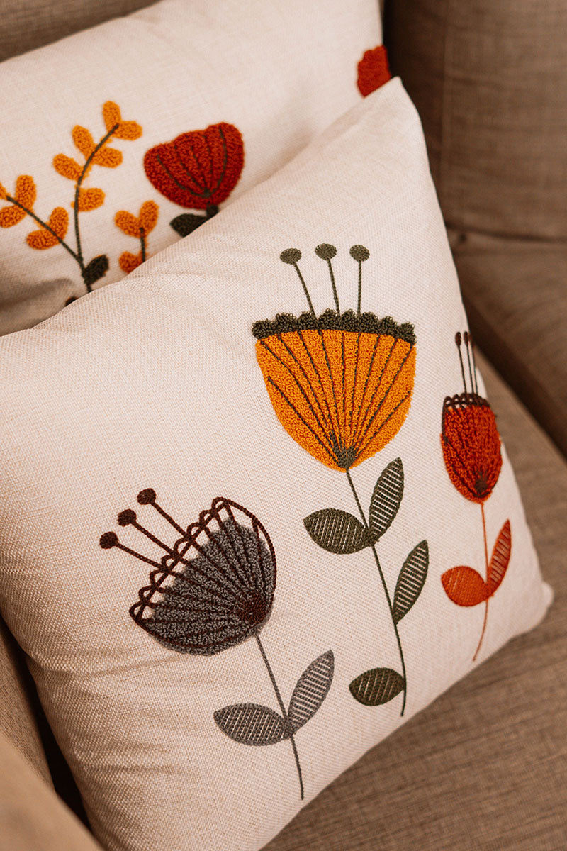 Embroidered floral cushion cover in beige fabric with colorful boho flowers on a blue sofa