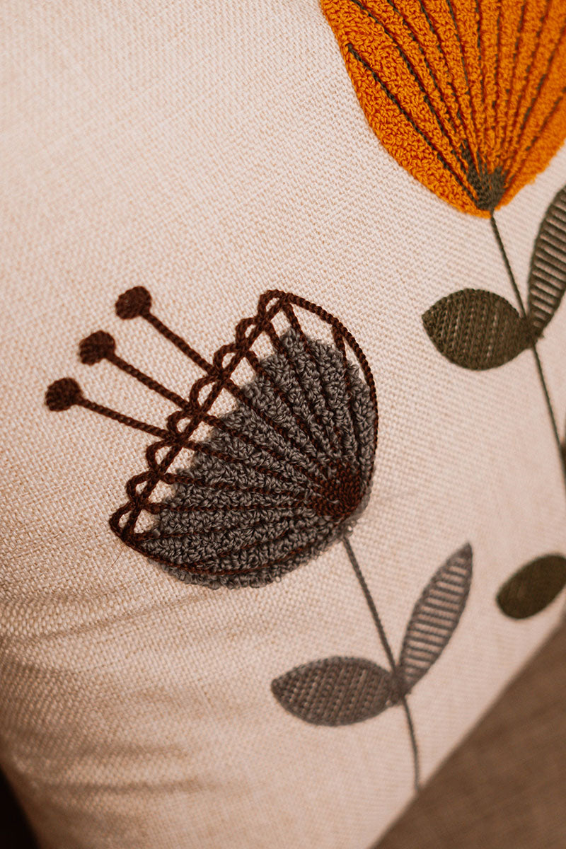 Embroidered floral cushion cover in beige fabric with colorful boho flowers on a blue sofa