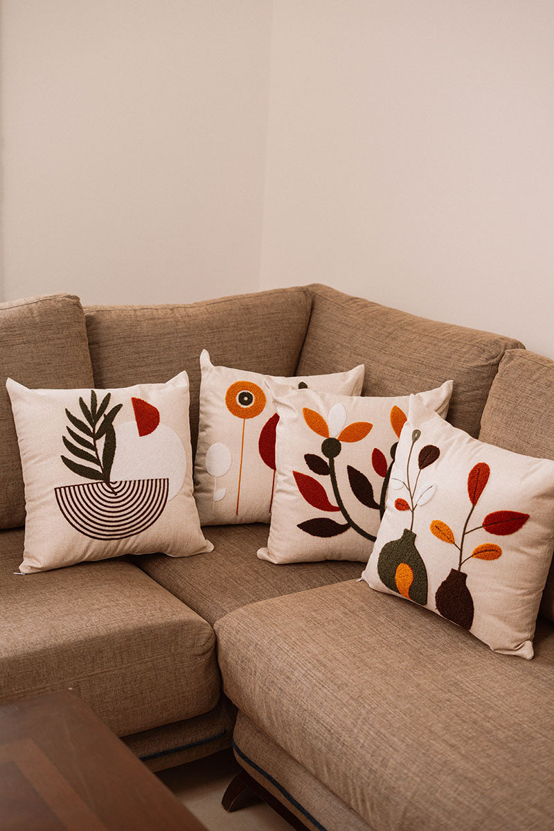 Beige cushion with embroidered vases and leaves in rust, orange, brown, and white on a blue sofa – Autumn Bloom Collection