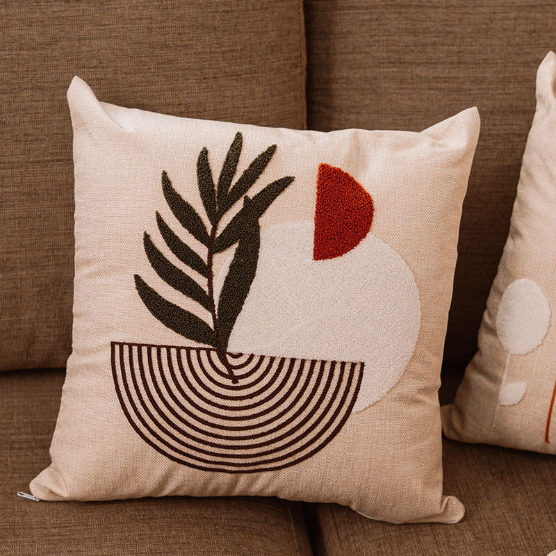 Beige cushion with embroidered palm leaf and geometric shapes in rust and green on a blue sofa – Autumn Bloom Collection