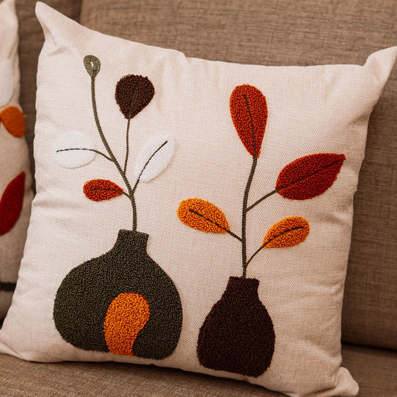 Beige cushion with embroidered vases and leaves in rust, orange, brown, and white on a blue sofa – Autumn Bloom Collection