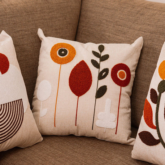 Beige cushion with geometric floral embroidery in rust, mustard, olive, and white on a blue sofa – Autumn Bloom Collection