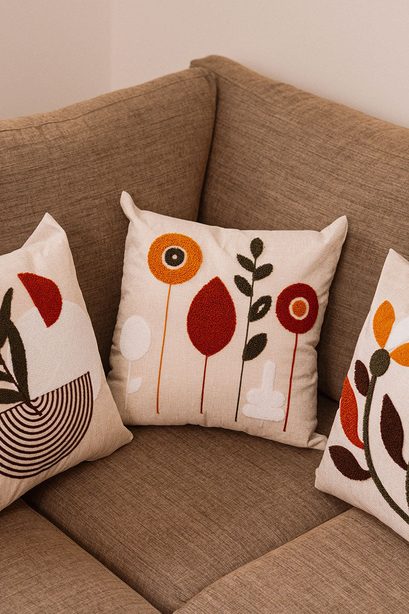 Minimal embroidered floral cushion cover with mustard, rust, and olive leaves on beige fabric, placed on blue sofa
