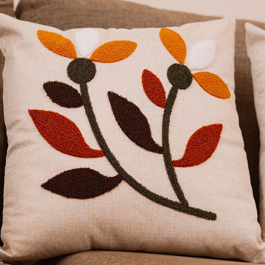 Minimal embroidered floral cushion cover with mustard, rust, and olive leaves on beige fabric, placed on blue sofa