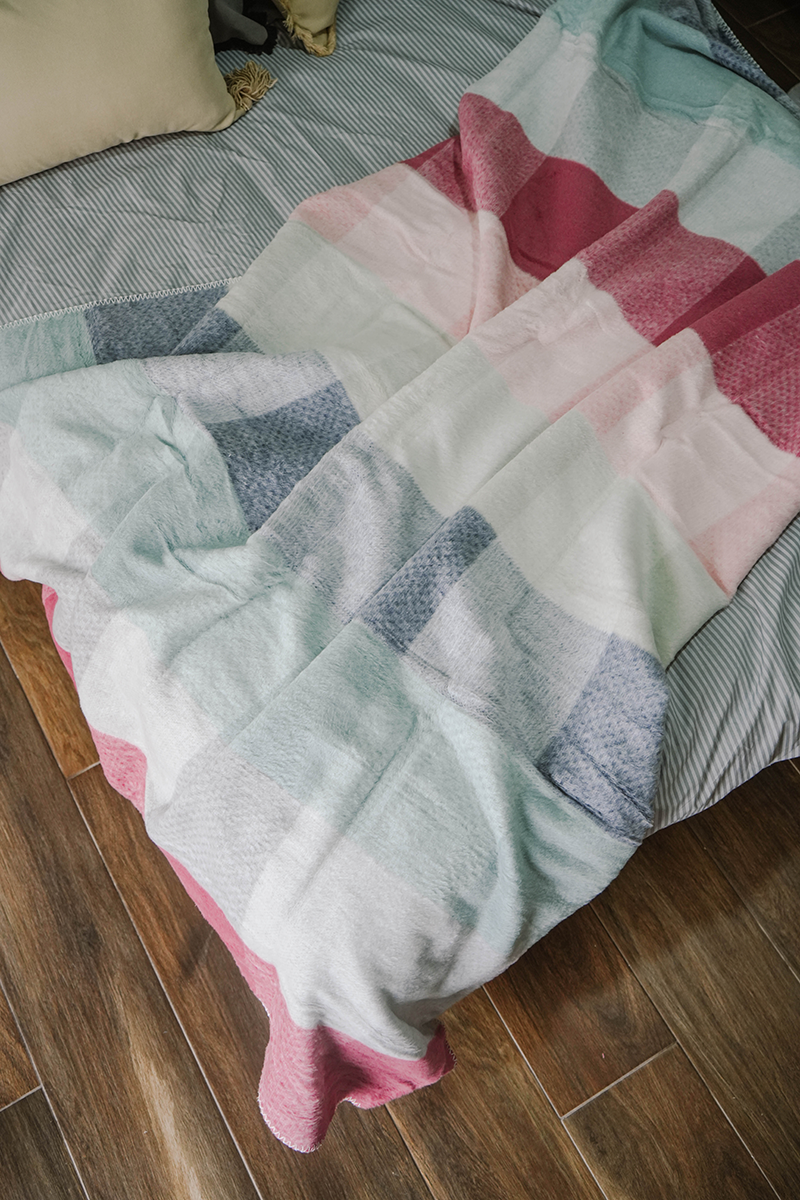 Pastel checkered fleece blanket in pink, grey, aqua, and white draped on ladder